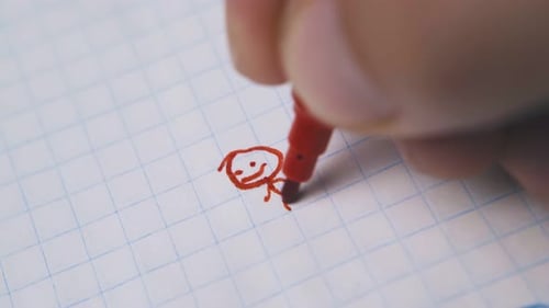 Junger Mann zeichnet einen lustigen Menschen mit rotem Stift auf Papier