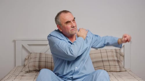 Mature Man Massaging Sore Shoulder on Bed