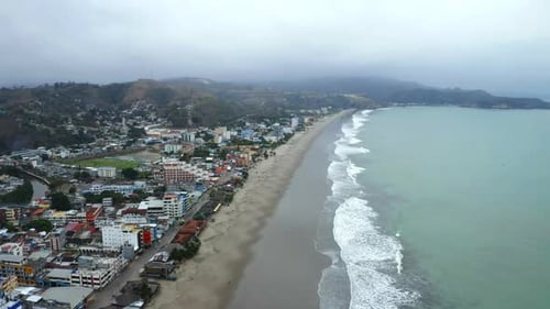 Vista aérea, seguindo uma praia ao lado de uma pequena vila com edifícios altos
