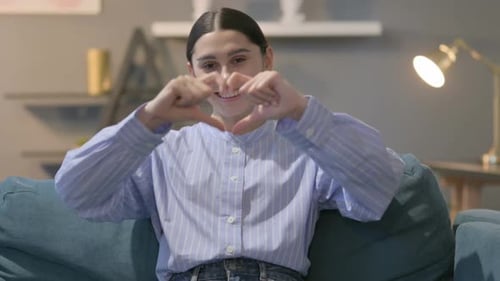 Woman Makes Heart Shape with Hands on Couch