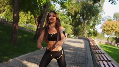 Young Woman Doing Squats in the Park Listening to the Music Breathing Slowly and Looking in the