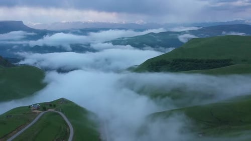 Vol de Drone au-dessus de champs verdoyants dans les montagnes dans les nuages et le brouillard.