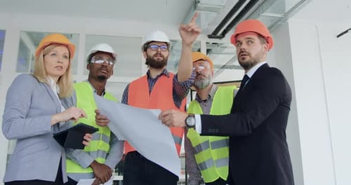 Equipo multirracial de ingenieros que discute los detalles del plan con los clientes en el sitio de construcción