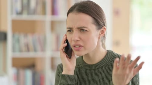 Upset Young Woman Talking on Smartphone Indoors