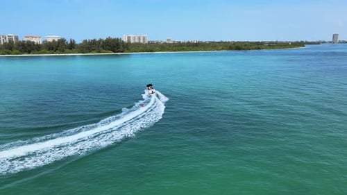 Following a boat in the ocean pulling people on an inflatable tube. The camera orbits around speedbo