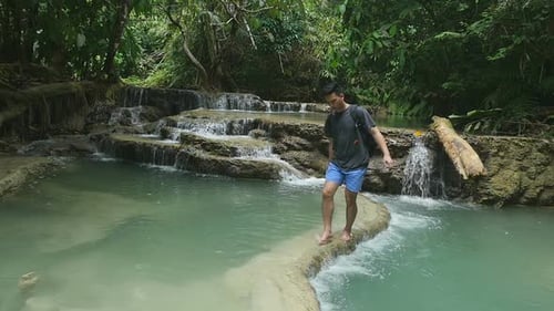 Man Walks Barefoot Near Tropical Waterfall