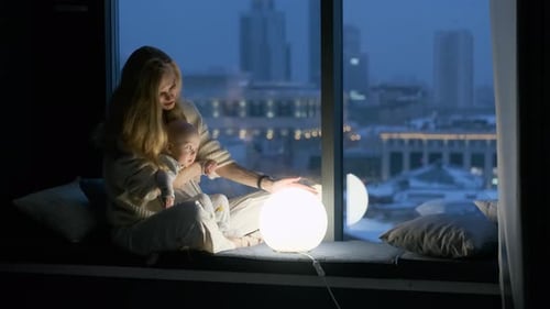 Mother and Baby Near Glowing Lamp at Night