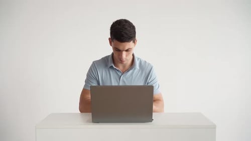 Handsome Man in Blue Polo Shirt Works for Laptop in Office on a White Background