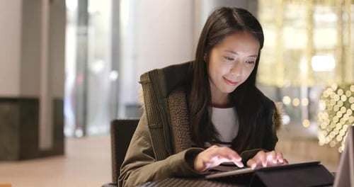 Woman use of tablet computer in coffee shop at night