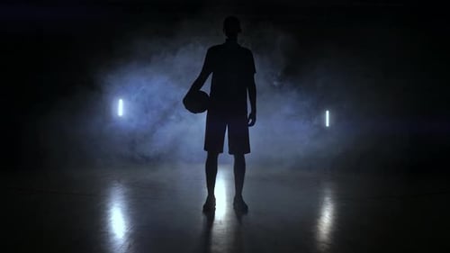 Die Silhouette eines Basketballspielers auf dunklem Hintergrund mit Rauch auf dem Basketballplatz