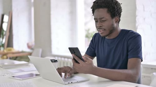 Young Adult Works at Desk with Laptop and Phone