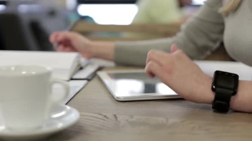 A business girl in a restaurant works with a tablet and drinks coffee.