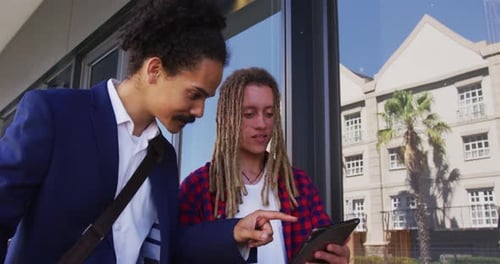 Two diverse male friends walking in the street using a digital tablet
