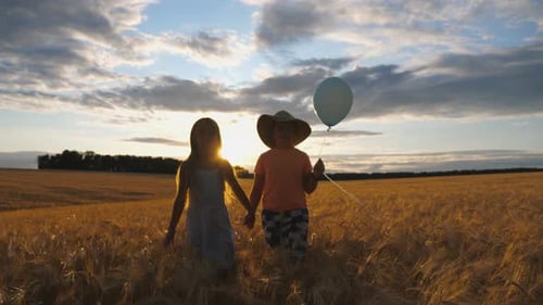 Couple of Cute Little Kids Holding Hands of Each Other Walking Through Wheat Field at Sunset