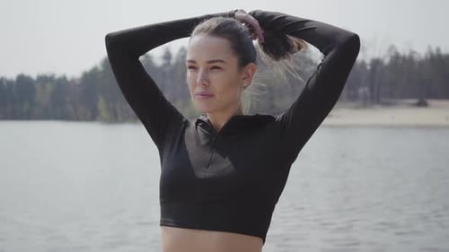 Woman Puts Hair in Ponytail at Lakeside