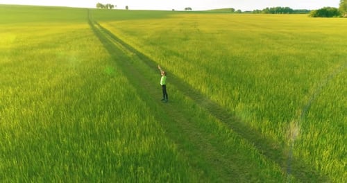 Sporty Child Standing in Green Wheat Field with Raised Hands Up