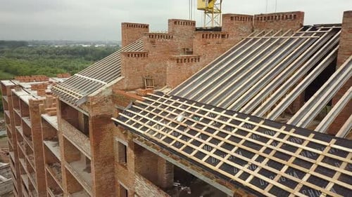 Aerial view of unfinished brick apartment building with wooden roof structure under construction.