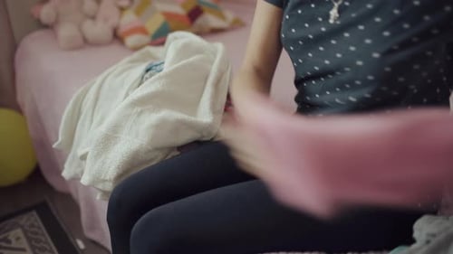 Woman Folds Baby Clothes on a Pink Bed