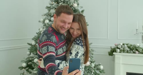 Happy Couple Taking Christmas Selfie by Decorated Tree