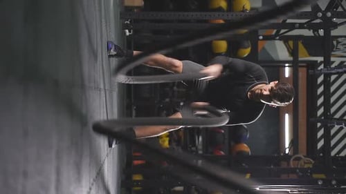 Hombre fuerte en pantalones cortos deportivos haciendo ejercicio con cuerdas de batalla en el gimnasio de crossfit