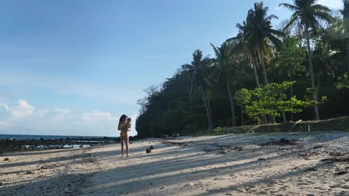 A Young Mother Walking on the Beach with Her Baby in Summer Time