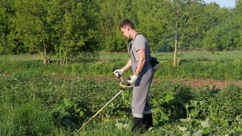 Man in a Working Uniform Mows Grass with a Trimmer