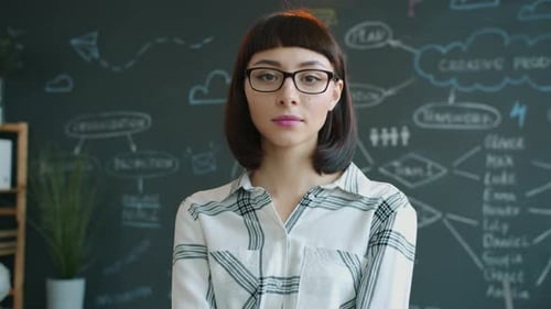 Portrait of Serious Young Woman Standing in Office with Chalkboard in Background