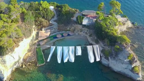 Isla camafeo en Grecia con playa y sábanas blancas volando en el cielo.