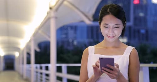 Woman Using Smartphone on City Bridge at Night
