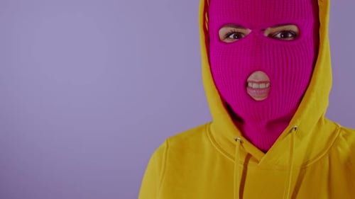 Nahaufnahme einer unkenntlichen Frau in rosa Sturmhaube zwinkert auf lila Hintergrund