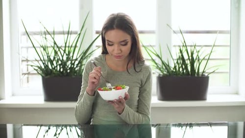 Woman Eats Salad at Table Near Window