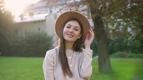 Happy Woman in Trendy Hat Looking at Camera with Sincerely Smile on the Background of Green Trees