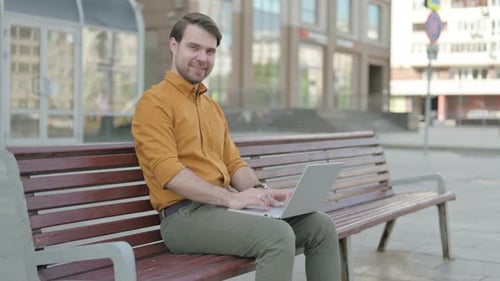 Man Working on Laptop on Bench in City