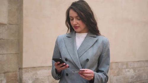 Woman Using Phone and Credit Card on Street