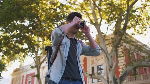 Young Attractive Handsome Man Tourist with Backpack Taking Photos on Vintage Camera in Old City