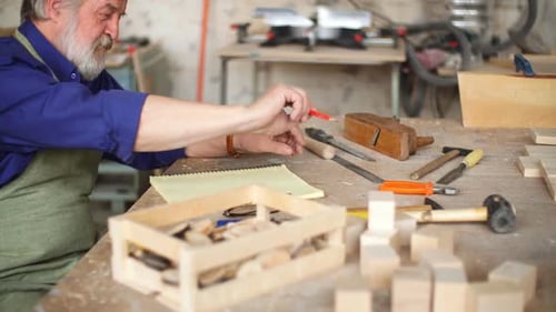 Senior Man Designs Wood Structure at Workbench