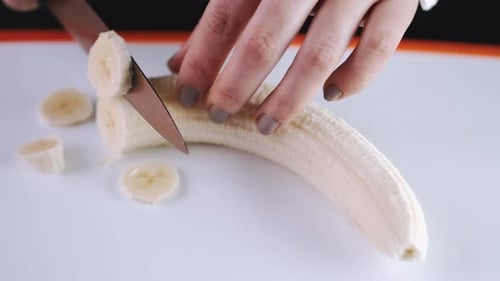 Hands Slicing Banana on Cutting Board