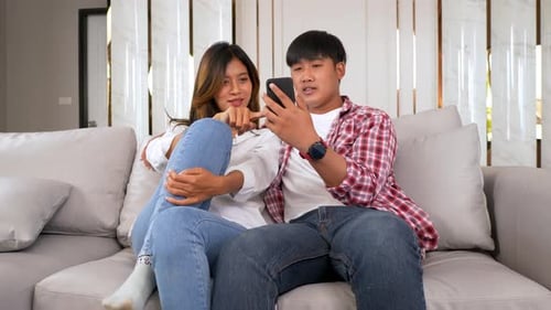 Smiling Couple Relaxing on Couch with Smartphone