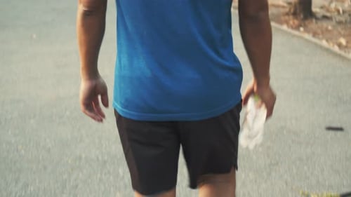 Young Asian man athlete walking and holding water bottle after running at the park.