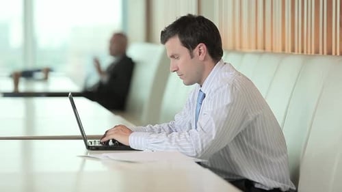 Geschäftsmann benutzt Laptop und schaut in die Kamera