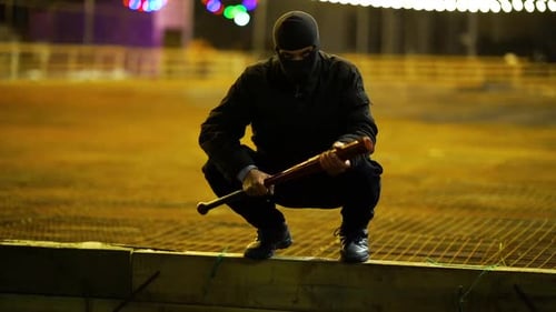 Masked Figure Squatting with Baseball Bat at Night