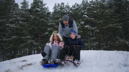 Active Weekend Happy Father Rodeln mit seinem Sohn und seiner Frau einen verschneiten Hügel im Winterwald hinunter