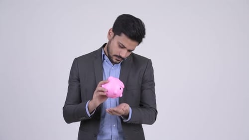 Young Bearded Indian Businessman Holding Piggy Bank and Shrugging