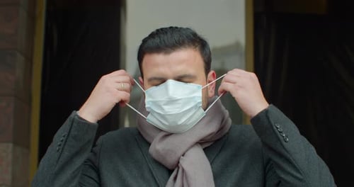 Young Man Out and About in the City Streets During the Day, Putting on a Face Mask Against Air