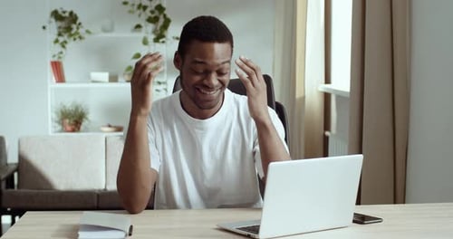 Man Works on Laptop at Desk Smiling Indoors