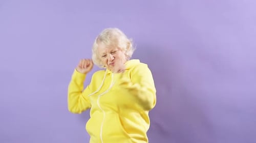 Joyful Senior Woman Dancing Energetically in Yellow Hoodie