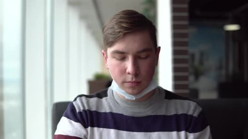 A Young Man Takes Off a Medical Mask and Eats a Burger, and Then Puts on a Mask. A Man Sits