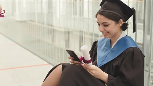Graduate Woman Sits With Diploma and Mobile Phone