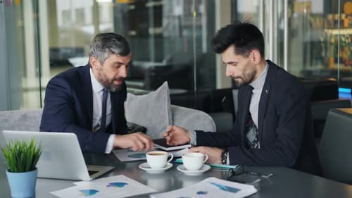 Entrepreneurs Arguing During Meeting in Cafe Discussing Charts Using Laptop