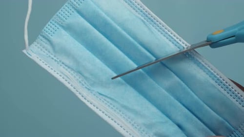 Cutting Surgical Mask with Scissors on Light Blue Background